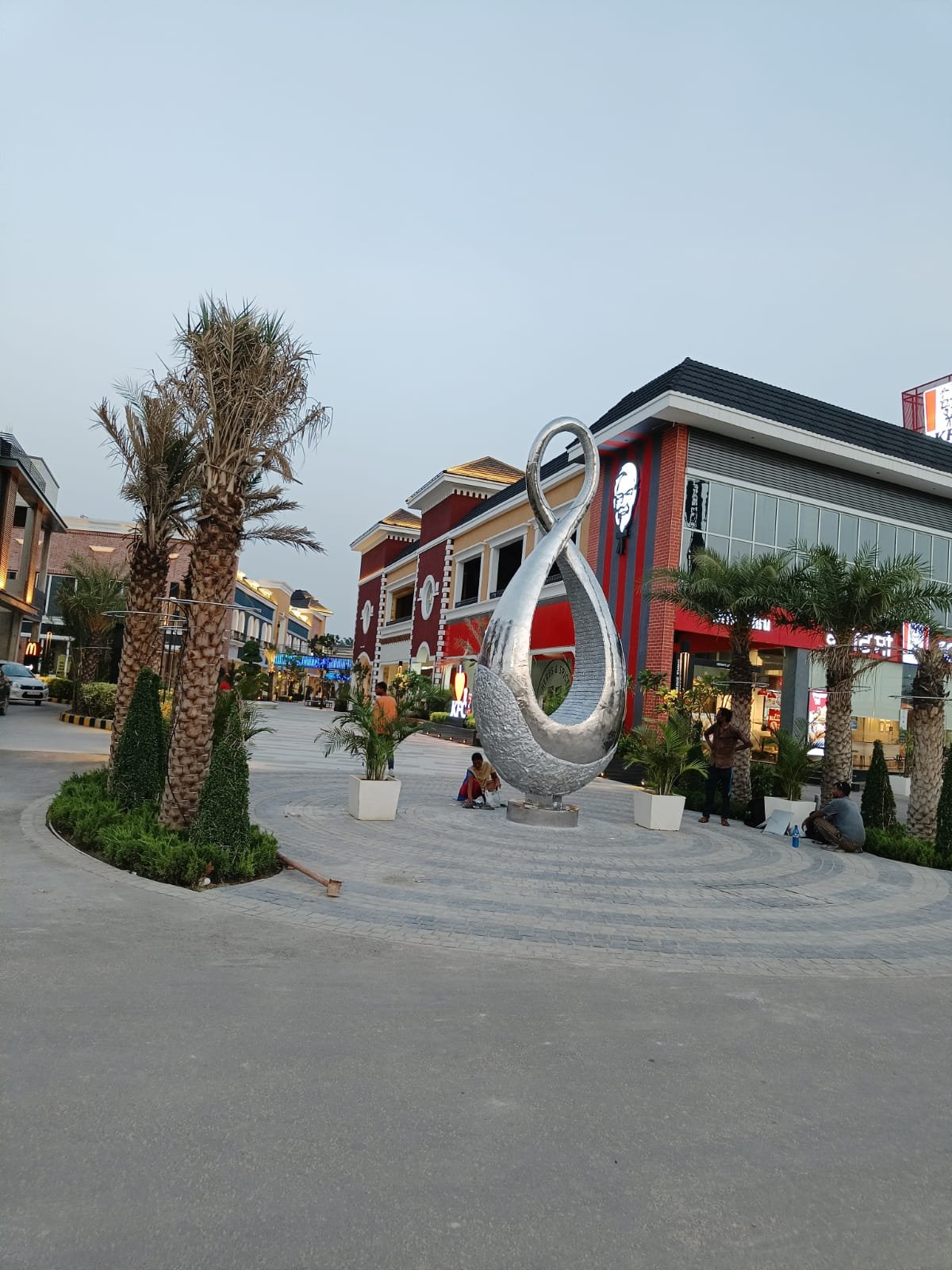 Mirror-polished stainless steel infinity sculpture on a landscaped roundabout at a shopping street