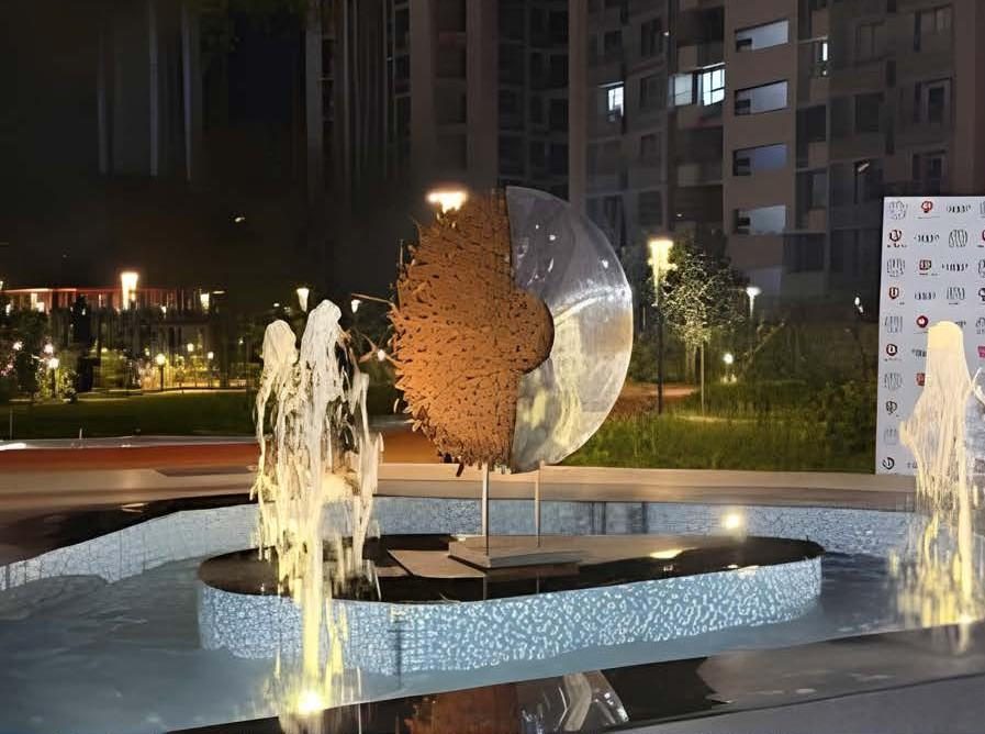 Mirror-finish steel and corten sculpture in a lit fountain at night